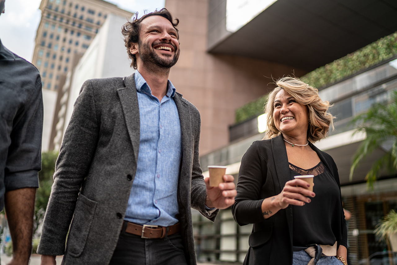 Two business professionals smiling and holding drinks in an outdoor setting