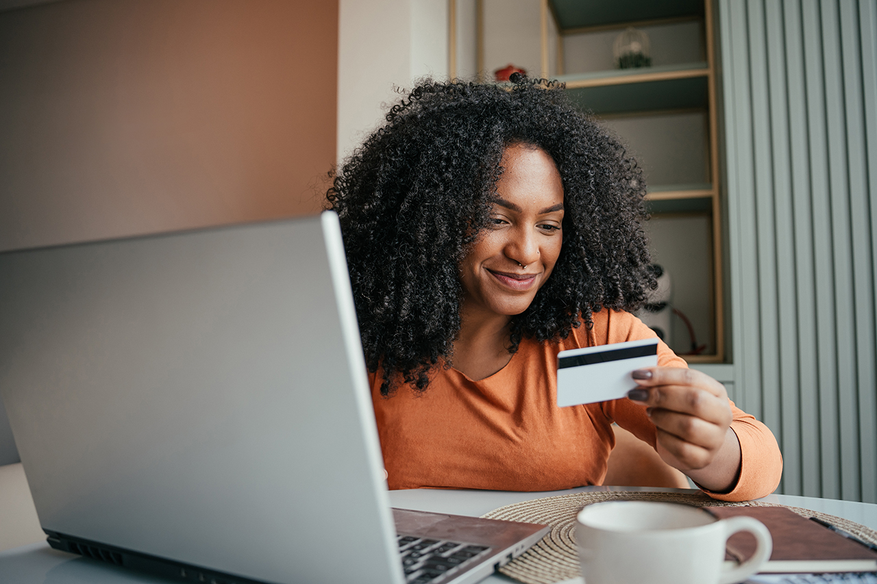 Woman sitting at a desk, holding a credit card while working on a laptop