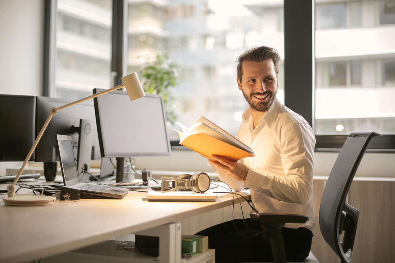 Man sitting at a desk with a book, smiling and enjoying his work